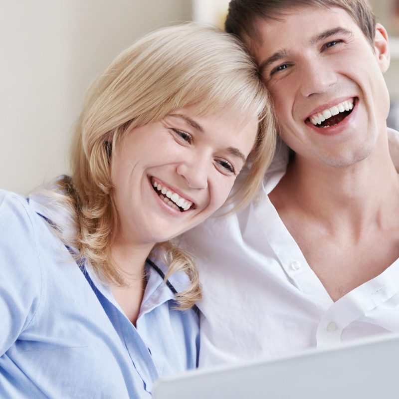 Laughing young couple with laptop at home