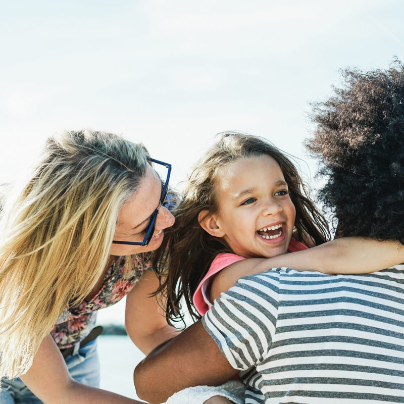 Happy family having fun on the beach - Multi-ethnic couple playing with cheerful daughter on summer time - Focus on kid face