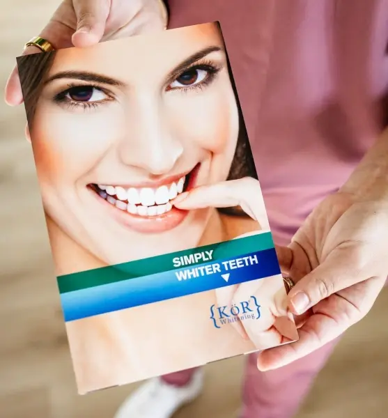 Patient smiling while holding a teeth whitening shade guide during a cosmetic dentistry consultation